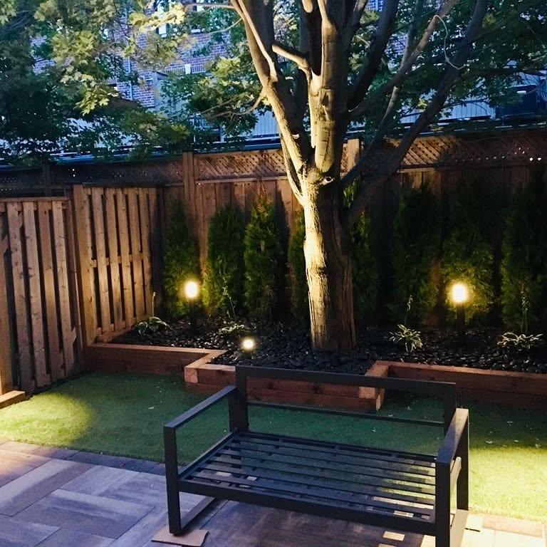 Backyard patio with warm landscape lighting along garden bed at night